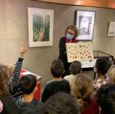 une bibliothécaire montrant un livre à des enfants dont une levant la main